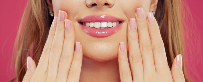 A woman with her hands on her face and pink lips.