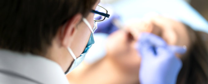 A dentist is wearing glasses and gloves while looking at the patient.