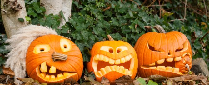 Three pumpkins with faces drawn on them sitting in the leaves.