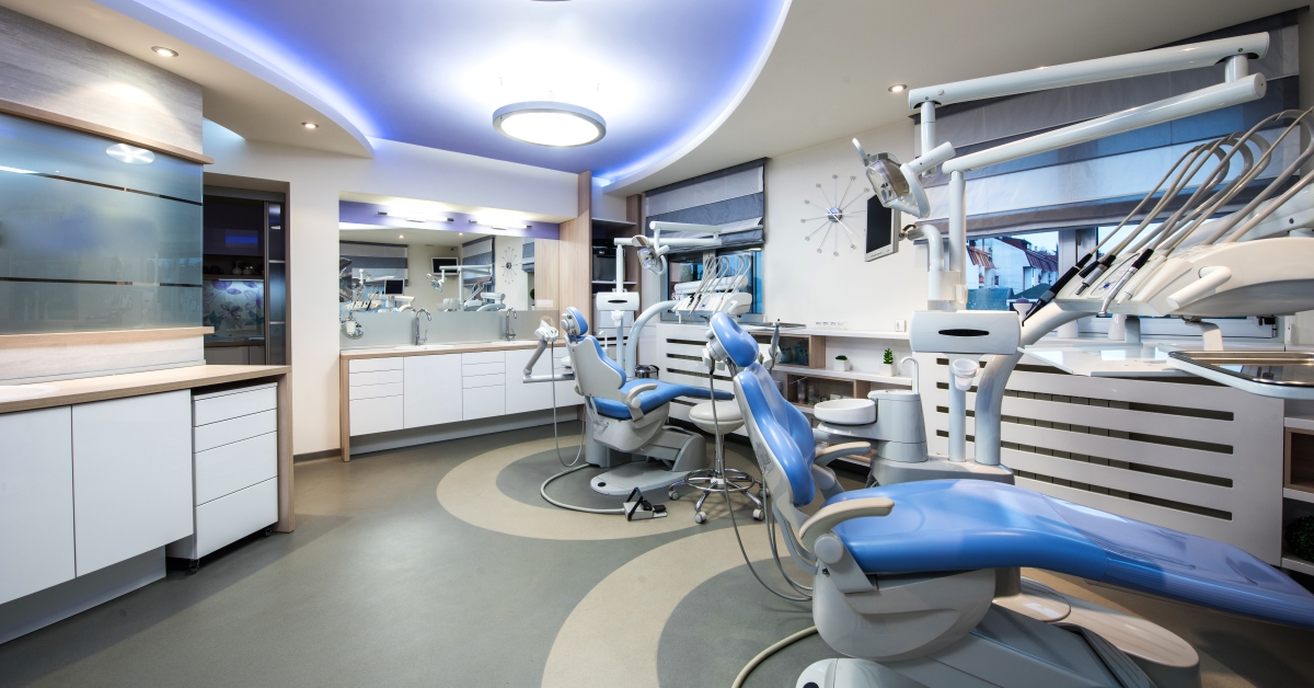 A dentist 's office with two blue chairs and a mirror.