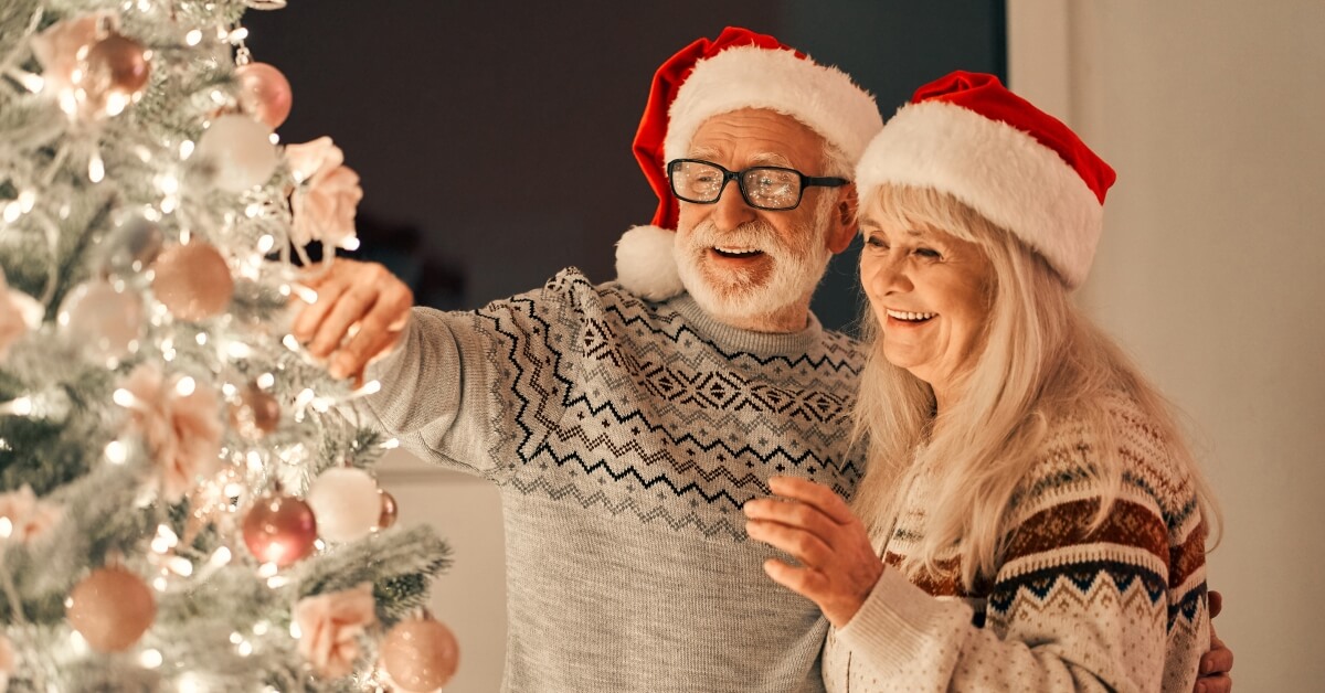 A man and woman in santa hats decorating christmas tree.