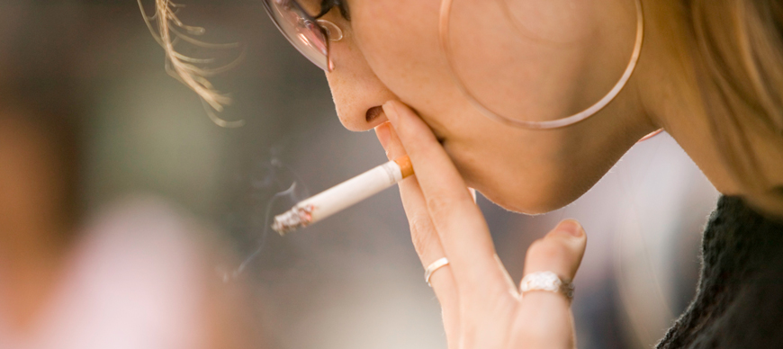 A woman is smoking a cigarette and looking down.
