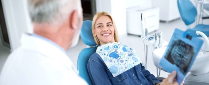 A woman sitting in the dentist chair smiling at an older man.