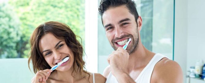 A man and woman brushing their teeth together.