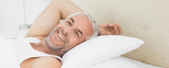 A man laying in bed with his head on pillows.
