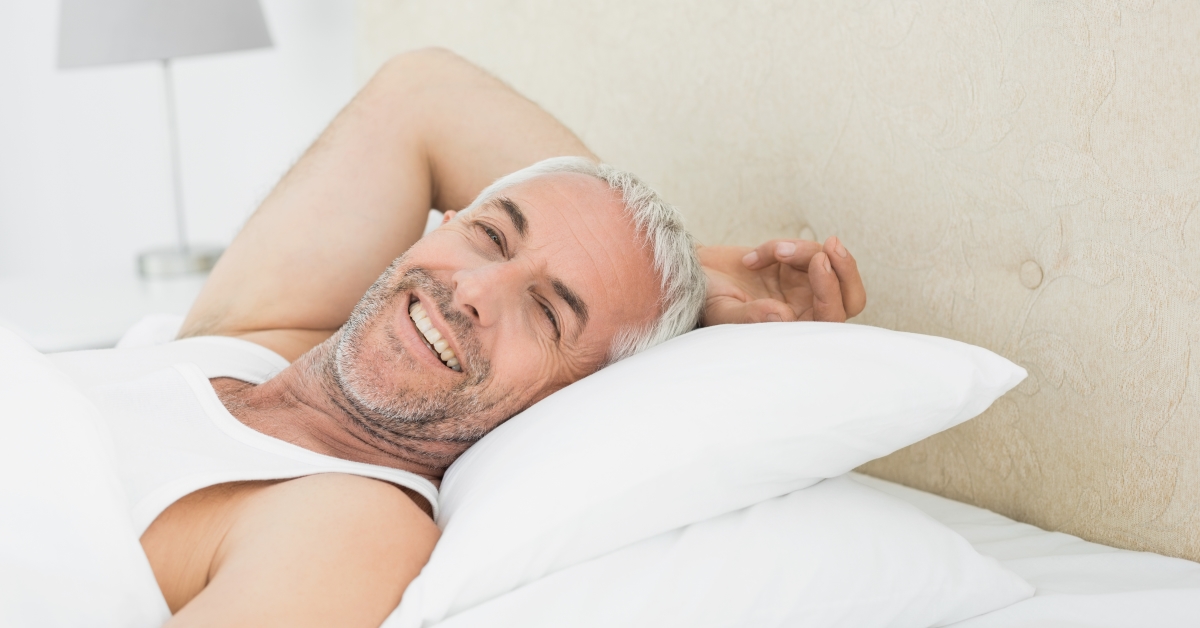 A man laying in bed with his head on pillows.