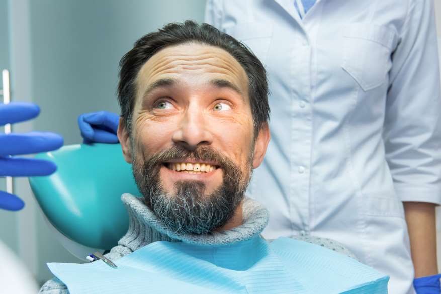 A man with long beard sitting in the dentist chair.