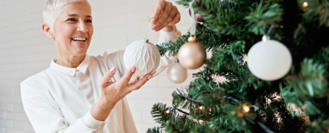 A woman is decorating the christmas tree with ornaments.