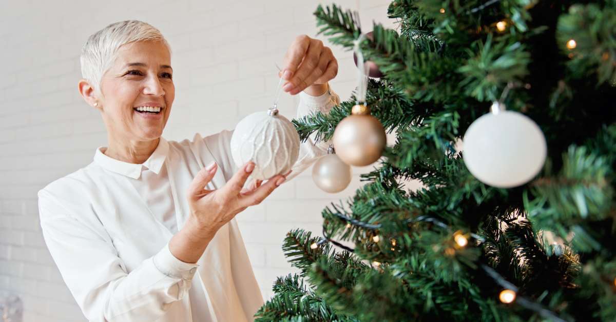 A woman is decorating the christmas tree with ornaments.
