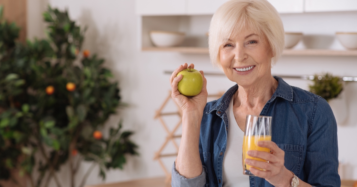 A woman holding an apple and drinking orange juice.