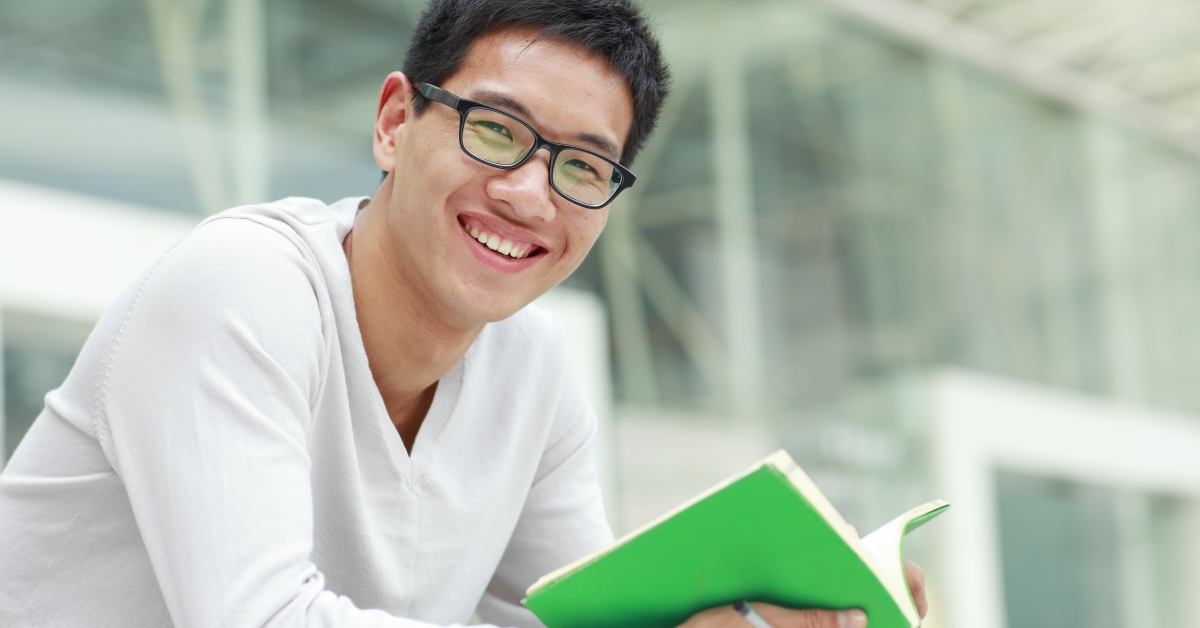 A man with glasses is smiling while holding a book.